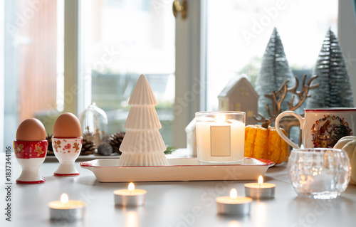 A Christmas decoration atmosphere with candle light, egg cup and mini Christmas tree in background.