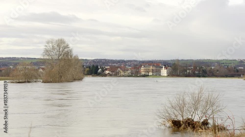 Flood in Dresden Mickten, Germany during winter 2023. The Elbe river overflows the floodplain areas. High water levels due to rainy weather. Trees and bushes are submerged in water.