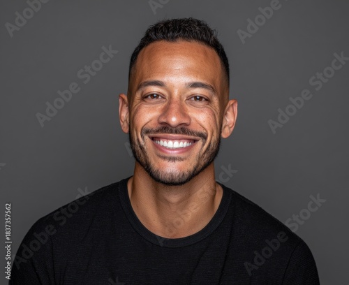portrait of smiling man in black t-shirt against plain gray background
