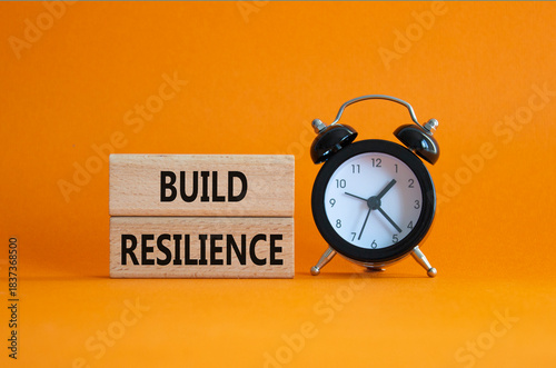 Build resilience symbol. Wooden blocks with words Build resilience. Beautiful orange background with alarm clock. Business and Build resilience concept. Copy space.