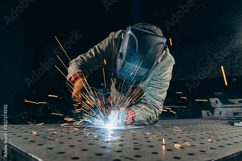 Welder in protective clothing welds metal parts in the workshop.