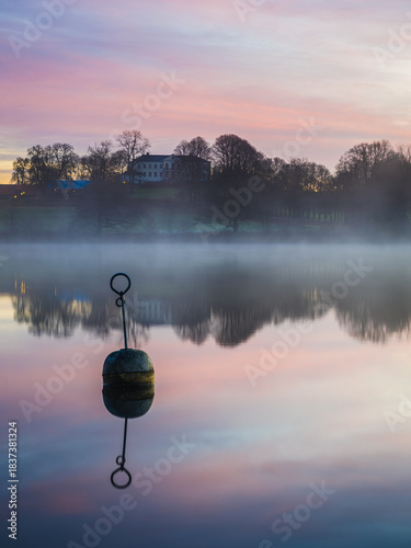 Bouy in still lake at sunrise in front of Naas castle in Sweden with mist on water
