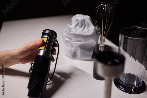 Black handheld immersion blender in professional kitchen setting, Kitchen expert demonstrating use of handheld immersion blender beside measuring tools and ingredients
