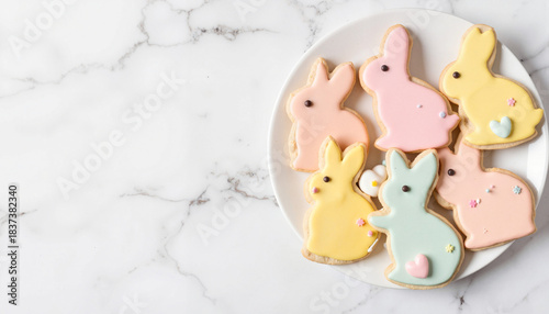 Pastel Easter bunny cookies on a white plate. Top view flat lay of decorated sugar cookies on a marble background with copy space