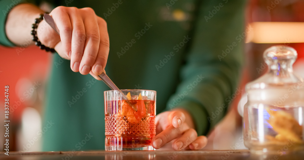 Obraz premium Garnishing cocktail. Alcoholic mix. Barman preparing refreshing drink with ice cube. Cold negroni served with orange fruit zest in glass.