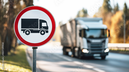 No trucks road sign in focus with a blurred freight truck driving on a highway in the background, highlighting transport regulations and traffic control.