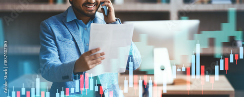 In a contemporary office, an Indian businessman holds papers while discussing a deal on his smartphone. His focused expression reveals active engagement in negotiations and decision-making.