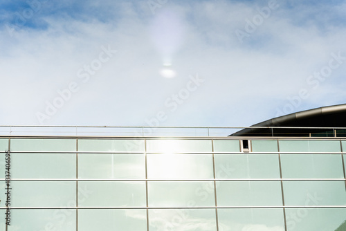 Fotografie Contemporary building exterior features large glass panels reflecting sunlight under a clear blue sky