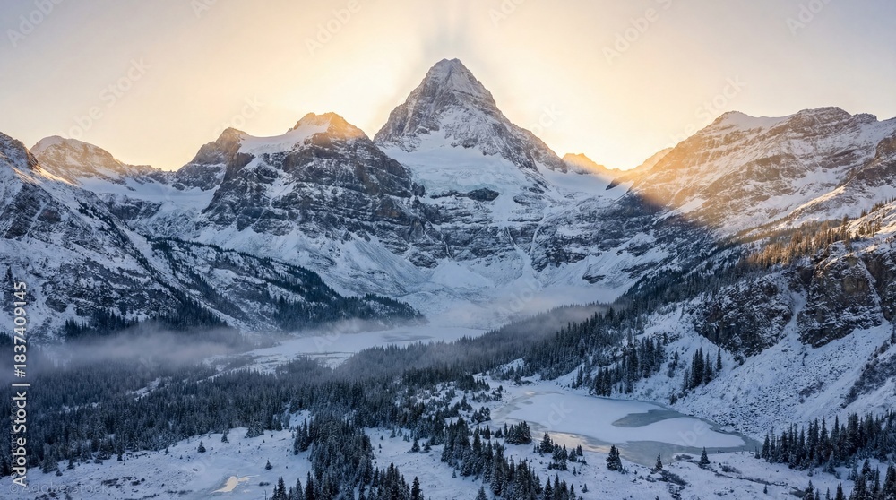 Obraz premium Snow-covered mountain peak rises above frozen lake and pine forest. Golden sunlight illuminates the summit creating a serene winter atmosphere. Ideal for travel and nature concepts.