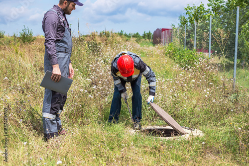 Two workers with a crowbar and a folder of documents open a water well in a rural area.