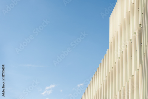 Minimalist building facade with vertical white panels set against a clear blue sky. Suitable for architecture, design, and urban development concepts.