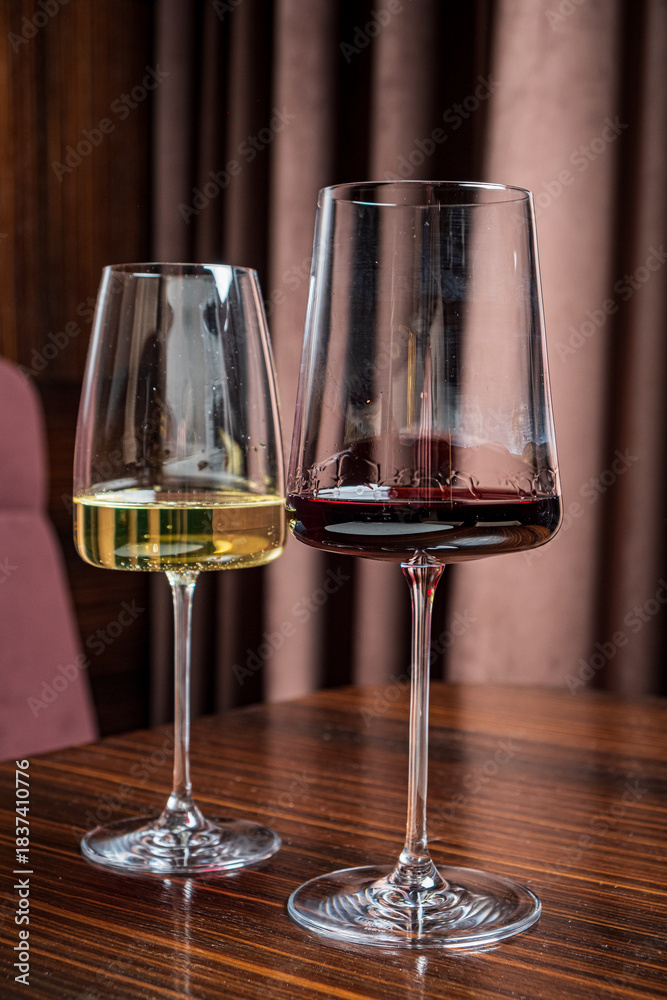 Naklejka premium Two beautifully shaped glasses hold fresh white and deep red wine, showcasing their vibrant colors