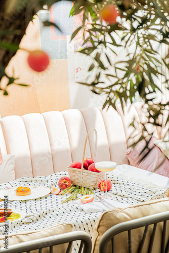 A delightful picnic is arranged on a patterned cloth, adorned with fruit, in a serene outdoor nook