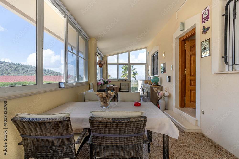 Fototapeta premium Enclosed terrace with wicker dining set and scenic mountain views