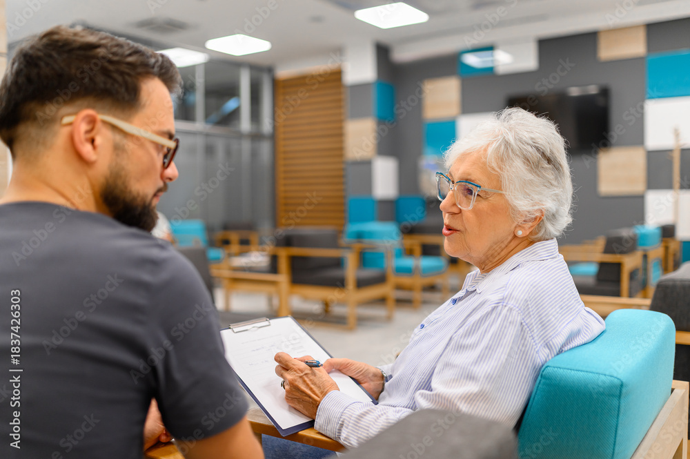 Obraz premium Senior woman discussing her medical records with male ophthalmologist while sitting in the hospital waiting room
