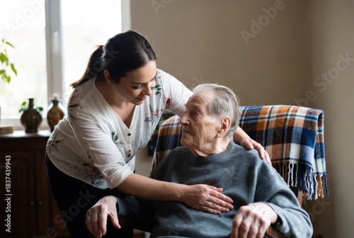 A caregiver interacts with an elderly man in a comfortable living room. They sit in chairs, engaging in conversation. Sunlight shines through the window, creating a warm atmosphere