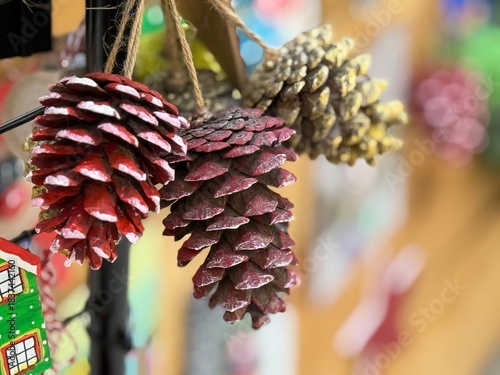 Close-up of a small bundle of pine cones with a blurred Christmas market background. Warm festive atmosphere, perfect for holiday designs, winter ads, and seasonal