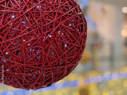 Close-up of a large red wicker Christmas ornament with glowing string lights inside. Festive holiday decor element for winter, New Year, and Christmas-themed designs