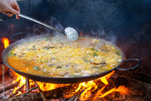 Traditional Valencian paella cooking process: distributing the rice evenly across the pan – Mediterranean cuisine in Spain.