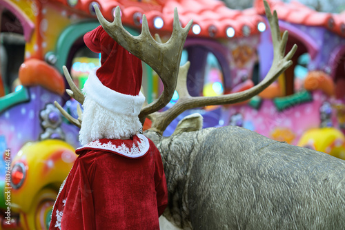 Holiday Santa Decoration Stands Beside Reindeer At Amusement Ride