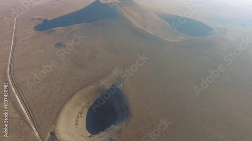 Aerial view of volcanic tuff ring cone crater and a barren geological sinkhole depression formation. Extinct volcano shows dry magma remains and crust features across an arid caldera from above.
