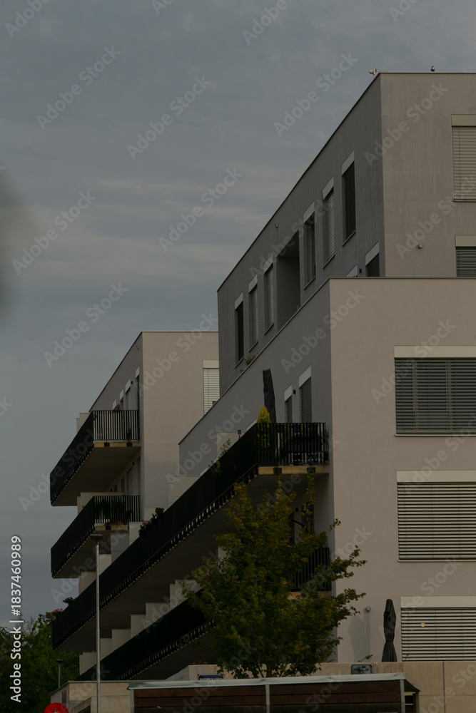 Fototapeta premium row of terraces and balconies in modern grey block, crisp horizontal lines with small trees below, industrial minimalism meets neighborhood calm, late light softening concrete edges and metal details