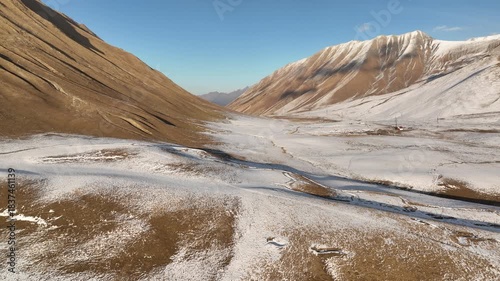 Aerial view of the winding Georgian Military Highway near Gudauri, Georgia. Mountain road surrounded by golden slopes and snowy peaks in early winter.
