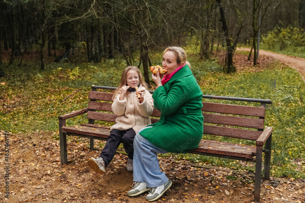 Fototapeta premium Sitting mother with daughter on park bench. Family talk, smile supports love, care, trust. Outdoor rest during walk adds bonding, childhood happiness, motherhood lifestyle, weekend leisure, comfort.