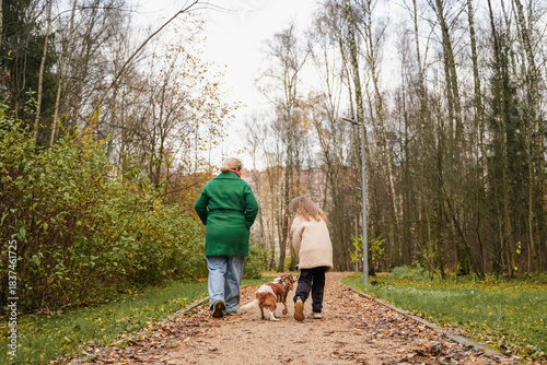 Walking mother with daughter, dog on park path. Family pet activity supports bonding, care, safety, healthy exercise. Outdoor weekend stroll with small canine fits city lifestyle, childhood joy.