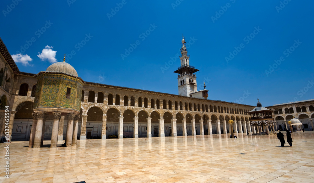 Naklejka premium The courtyard of the Umayyad Mosque in Damascus, showcasing historic Islamic architecture, marble flooring, and elegant arches. A cultural and religious landmark reflecting heritage, spirituality, an