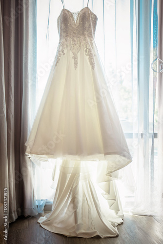 Hanging White wedding Dress gown against a window