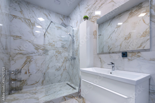 The modern bathroom is decorated with marble tiles, with a spacious shower cabin and a stylish cabinet with sink.