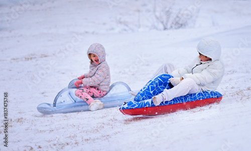 Joyful Children Sledding on Inflatable Sleds During Snowfall – Winter Fun, Outdoor Play, and Active Childhood Moments