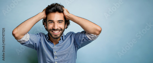 25/30 year old man with curly brown hair with a wide smile and a light blue shirt, looking at the camera with a happy and surprised expression.