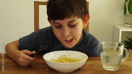 Boy eats noodles at the kitchen