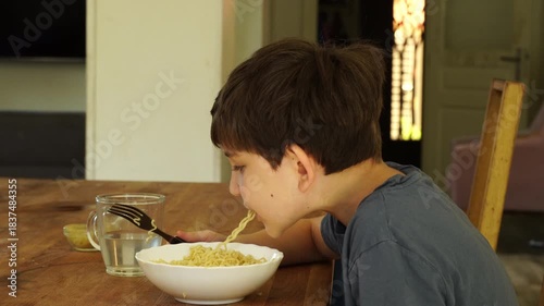 Boy eats noodles at the kitchen