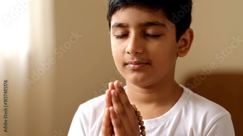 Young boy with eyes closed, hands joined in prayer, holding rosary beads