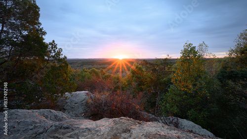 Glistening sunrise over rocky outcrop showcasing vibrant colors in the Illinois skyline, where nature awakens as sunshine pierces through scattered clouds, illuminating the landscape with golden rays