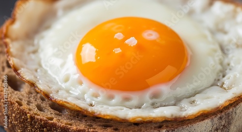 A close-up shot of a perfectly fried egg with a vibrant orange yolk and crispy white, seasoned with salt, resting on a slice of dark toast.