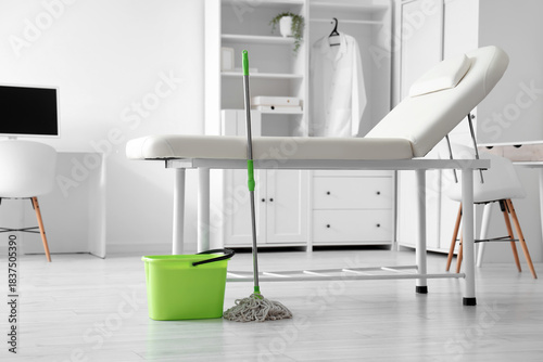 Clean medical examination room with mop and bucket, sanitation equipment near...