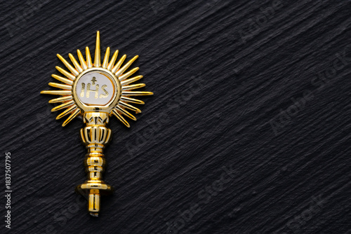Golden liturgical IHS ornament with a shiny design and metallic finish, highlighted against a textured black background