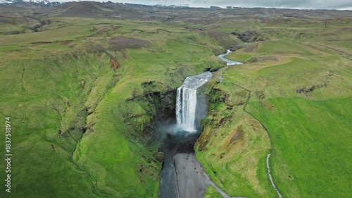Wide aerial drone view of Skogafoss waterfall and coast Iceland. 4K cinematic video shows iconic cascade and green landscape.