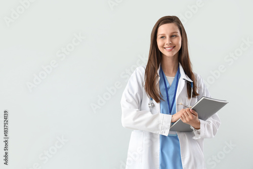 Female medical intern with notebook on light background