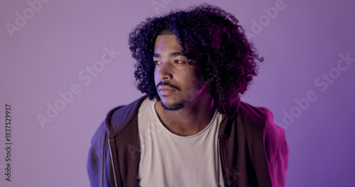 Studio portrait of a young African American man with curly hair looking away against a purple background. This image is suitable for fashion beauty and lifestyle concepts.