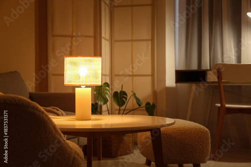 Interior of night living room with sofa, folding screen and glowing lamp on coffee table