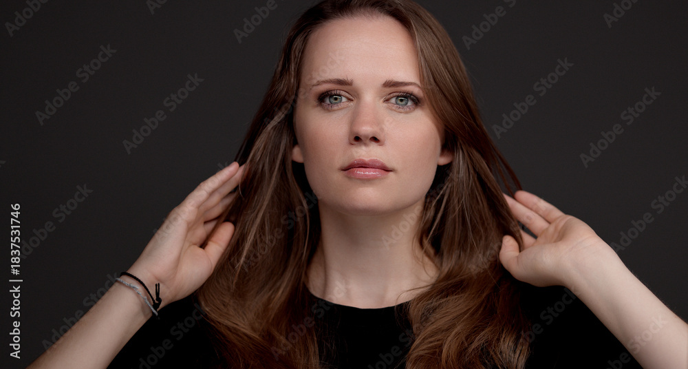 Fototapeta premium Studio portrait of a beautiful woman with long brown hair and natural makeup on dark background. This image is suitable for fashion beauty and commercial projects.