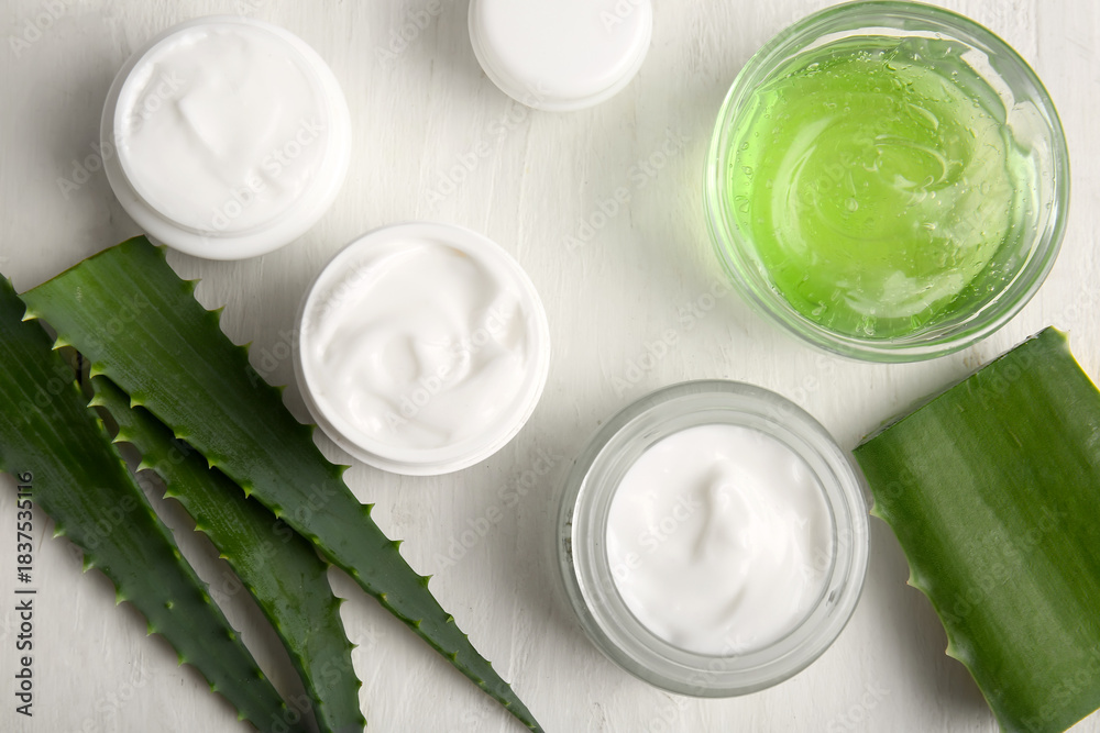 Naklejka premium Jars of cosmetic cream and glass bowl of gel with aloe vera leaves on white wooden background