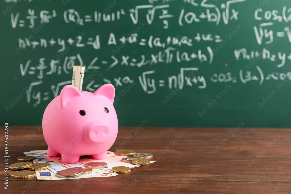 Fototapeta premium Piggy bank with money on table near green blackboard. Student loan concept