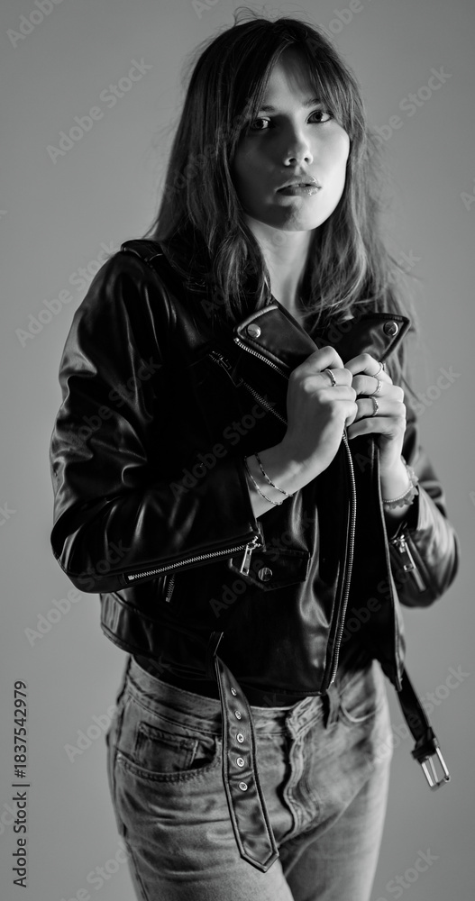 Obraz premium Monochrome studio portrait of a young woman wearing a leather jacket and jeans. This image is suitable for fashion beauty and style concepts.