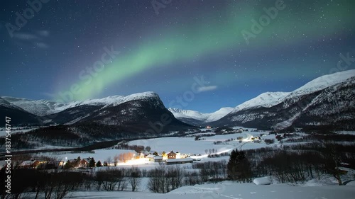 Aurora borealis lights up the night sky over snow-covered mountains and a small village below